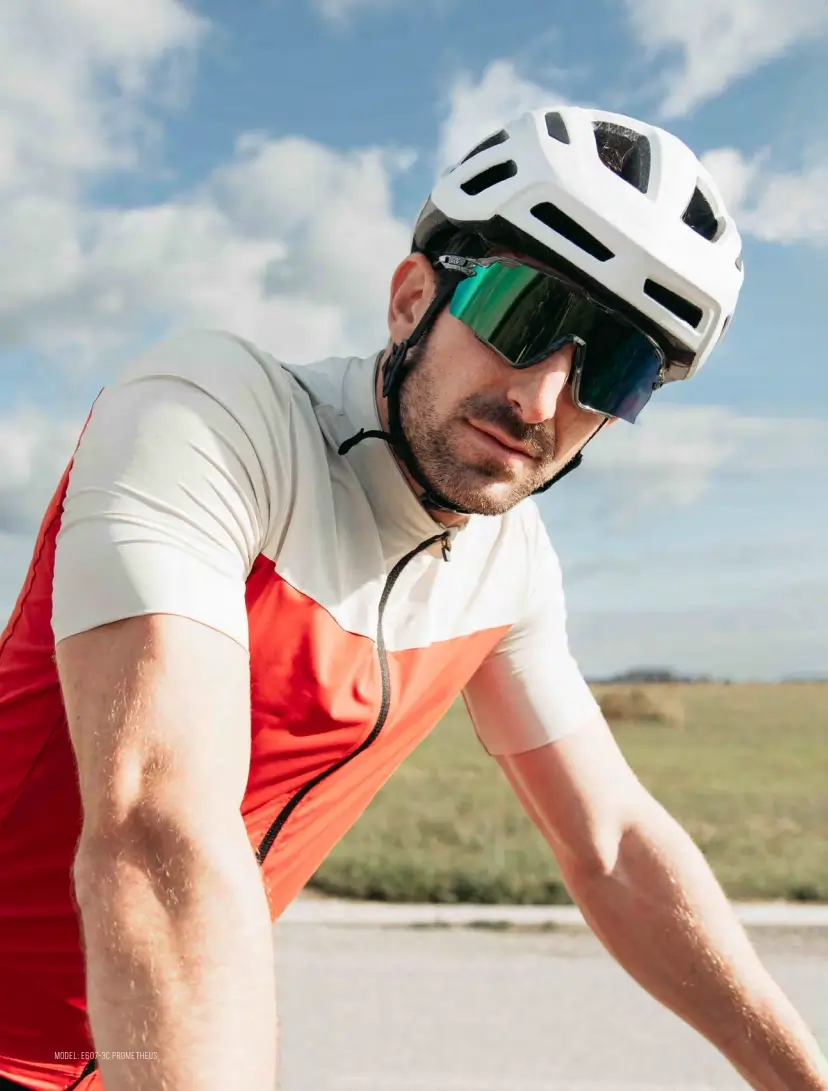 Cyclist wearing a white helmet and mirrored sunglasses, in a red-and-white cycling kit on a sunny outdoor road.
