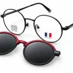 Two pairs of round glasses on a white background: black metal prescription frames with a crest sticker and a pair of red-and-black sunglasses with dark lenses.