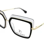Oversized square eyeglasses with black, clear, and gold frame accents; gold temples with Eva Minge branding visible.